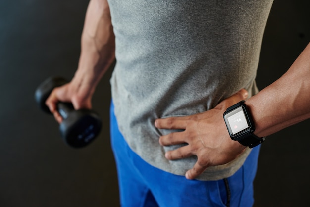 Unrecognizable man with smart watch holding dumbbell
