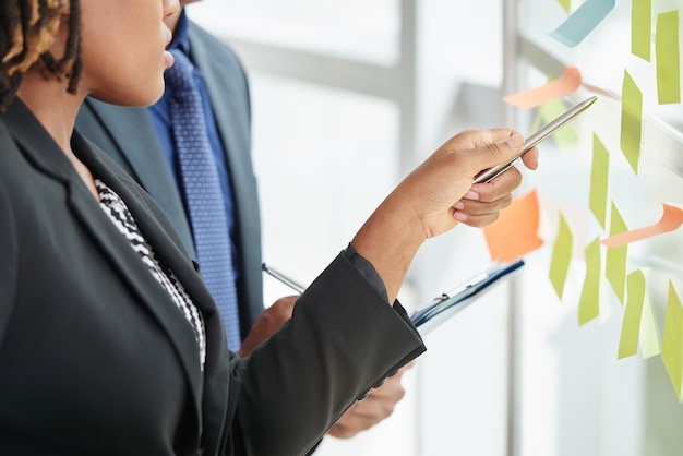 Unrecognizable man and woman in business suits looking at sticky notes on window