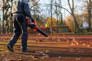 Free photo unrecognizable man working with handheld leaf blower while leaves curling and glowing around back