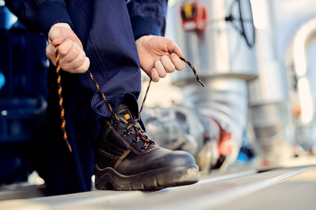 Unrecognizable manual worker typing shoelace at construction site