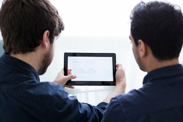 Unrecognizable men looking at graph on tablet