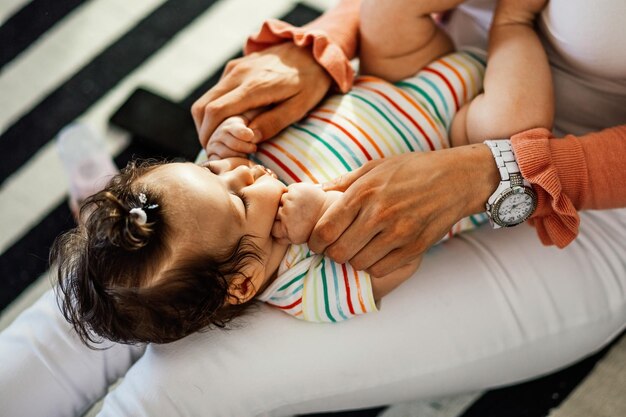 Unrecognizable mother having fun with her baby daughter while playfully squishing her cute cheeks