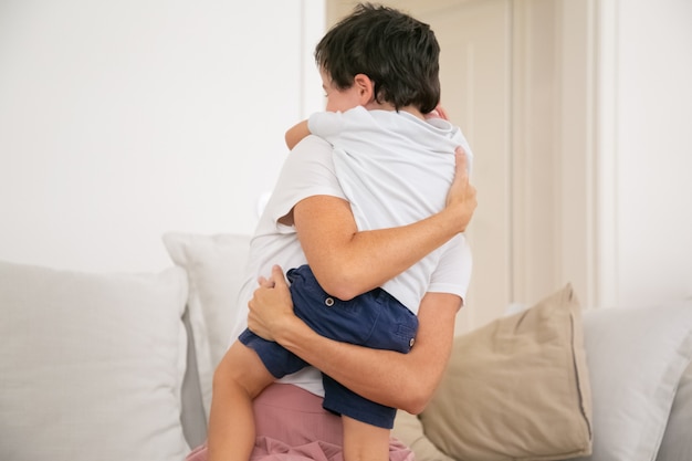 Unrecognizable mother hugging or embracing lovely son with love.