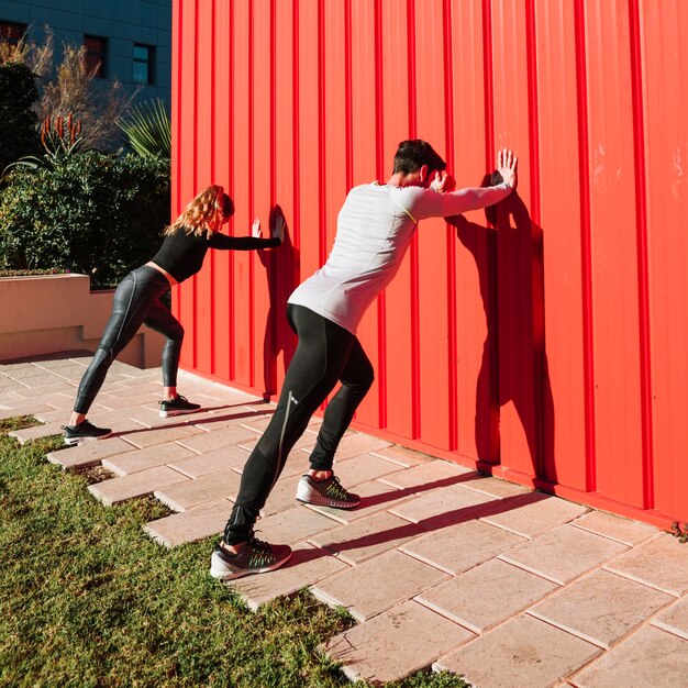 Unrecognizable people exercising near red wall