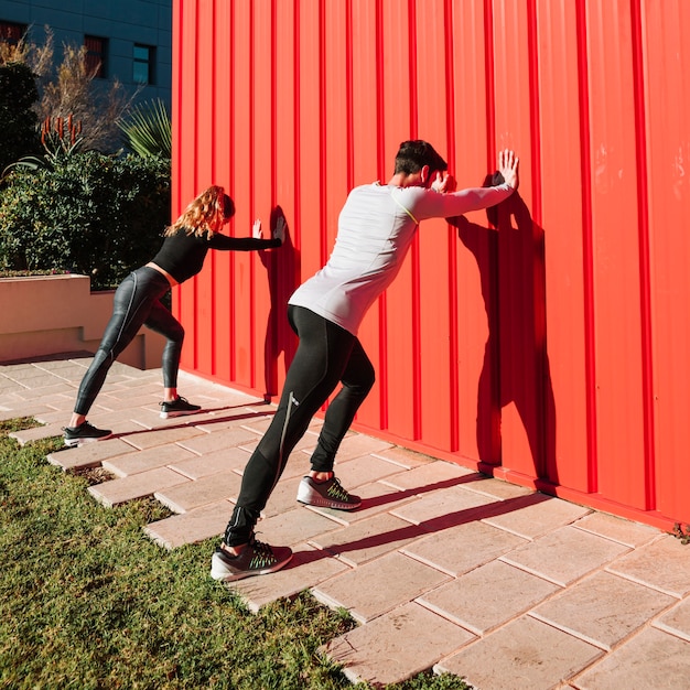 Unrecognizable people exercising near red wall