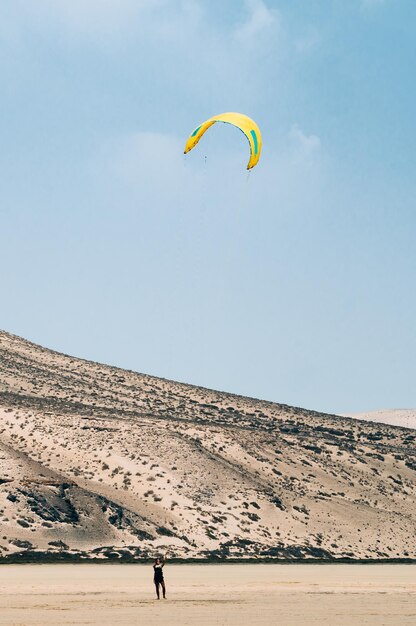 Unrecognizable people with paragliders on sandy terrain