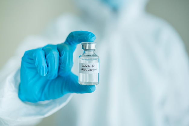 До неузнаваемости врач-специалист в медицинском костюме сиз демонстрирует вакцину против коронавируса sars 2019-ncov или мрнк covid-19. использование средств индивидуальной защиты или костюма сиз от коронавируса - пандемия covid-19.