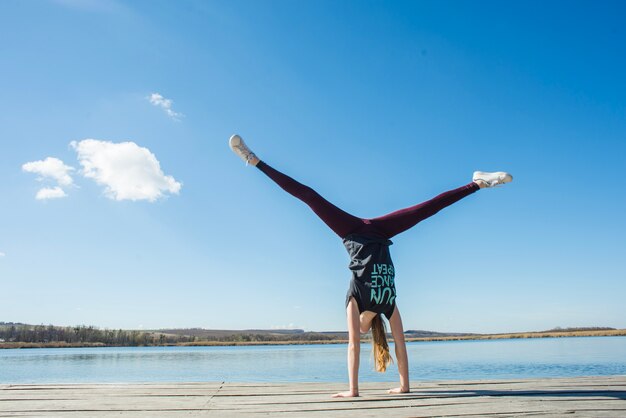 Unrecognizable teenager doing handstand on pier