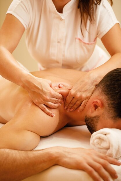 Unrecognizable therapist massaging man's shoulders during spa treatment