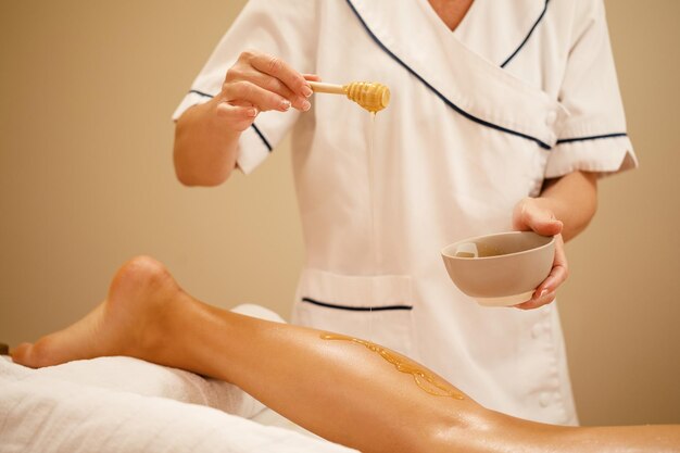 Unrecognizable therapist pouring honey while massaging woman's leg at spa salon