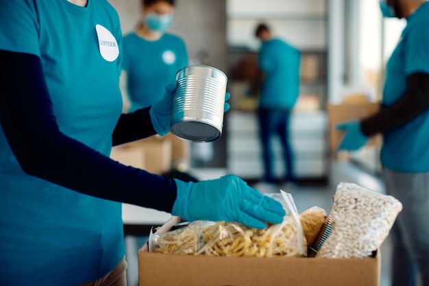 Unrecognizable volunteer packing donated food in cardboard box