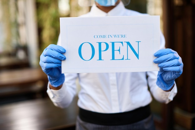 Unrecognizable waitress holding open sign at outdoor cafe