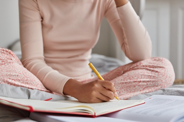 Free photo unrecognizable woman dressed in casual nightwear, writes in notebook, has inspiration for studying.