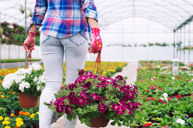 Unrecognizable woman florist carrying pots and flowers at plant nursery garden