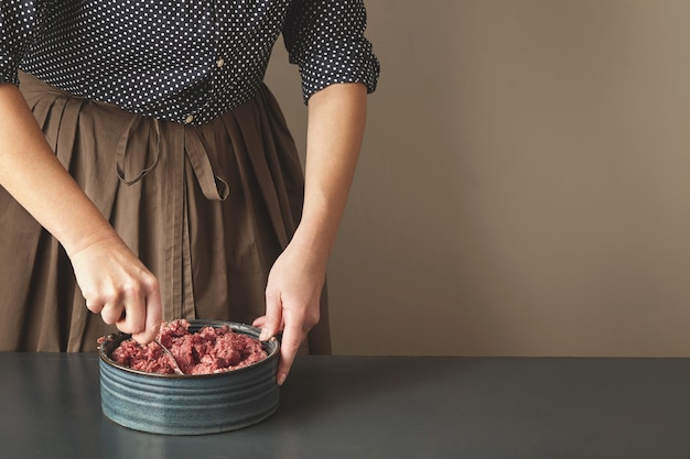 認識できない女性は、側面に分離されたビンテージテーブルのセラミックブルーボウルに鋼のスプーンでミンチ肉とスパイスを混ぜる