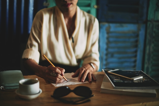 Unrecognizable woman sitting in cafe and drawing on napking