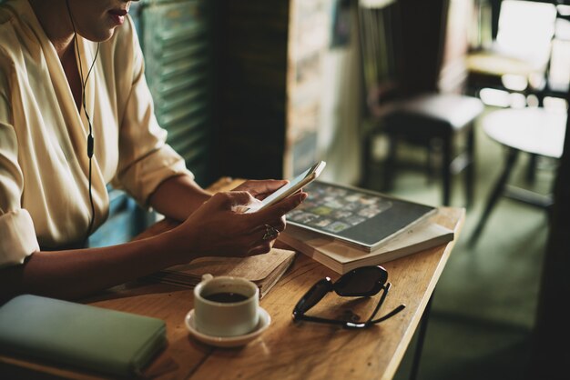 Unrecognizable woman sitting in cafe and listening to music on smartphone