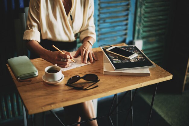 Unrecognizable woman sitting at table in cafe and writing on napkin