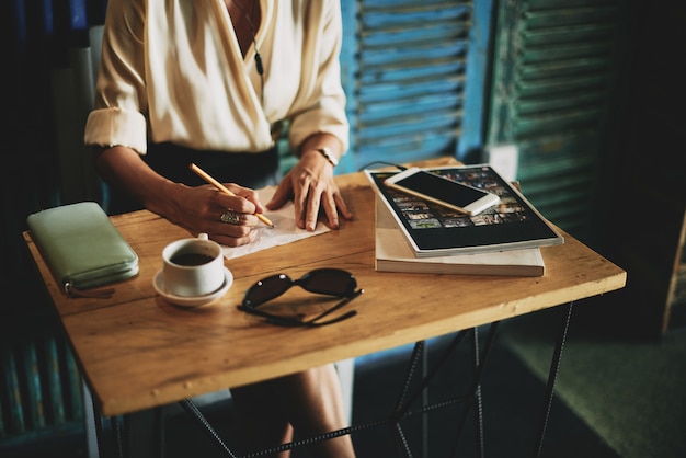 Unrecognizable woman sitting at table in cafe and writing on napkin