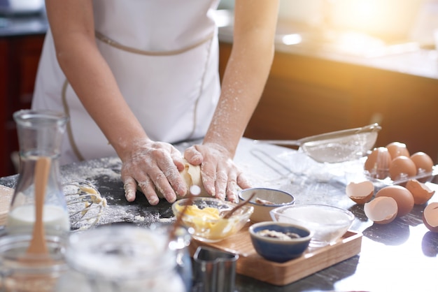 Unrecognizable woman standing at kitchen table and kneading dough by hand