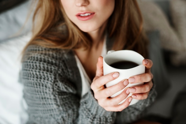 Unrecognizable woman with coffee mug on bed