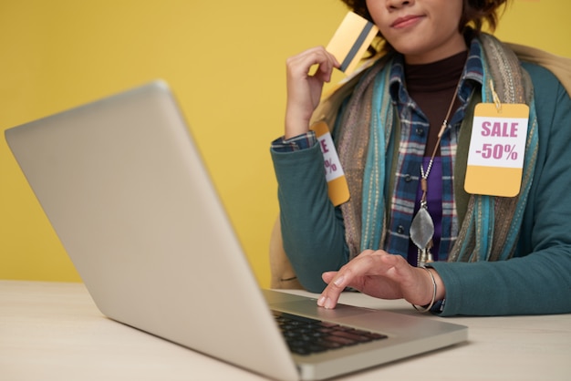 Unrecognizable woman with credit card using laptop and wearing scarf with discount labels