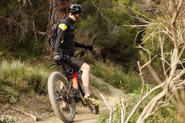 Unrecognizable young mountain biker in black cycling clothing keeping foot on pedal