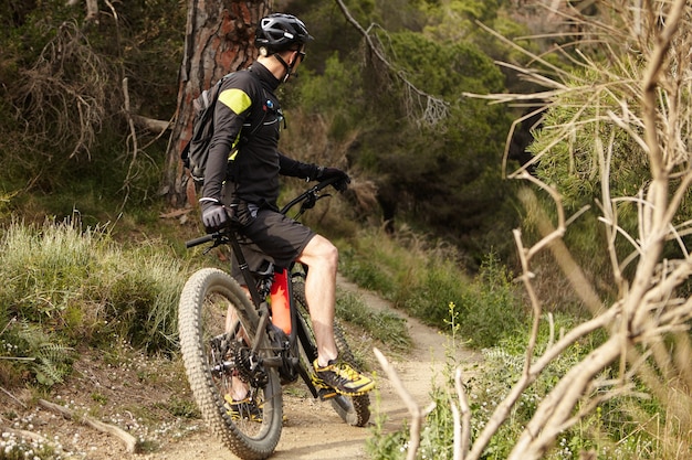 Unrecognizable young mountain biker in black cycling clothing keeping foot on pedal