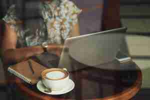 Free photo unrecognizable young woman sitting at table in cafe and working on laptop