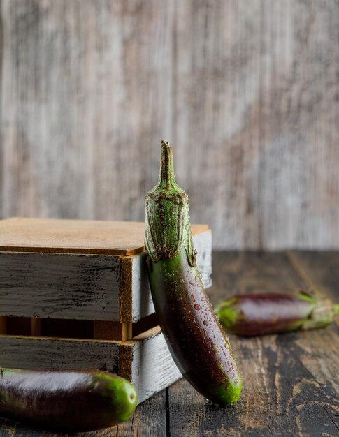 Unripe eggplants with wooden box side view on a wooden