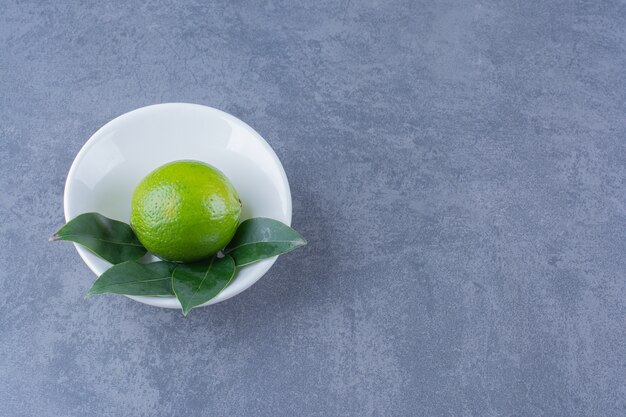 Unripe lemon in a bowl on marble table.