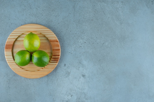 Unripe lemons on a wooden plate , on the marble table. 