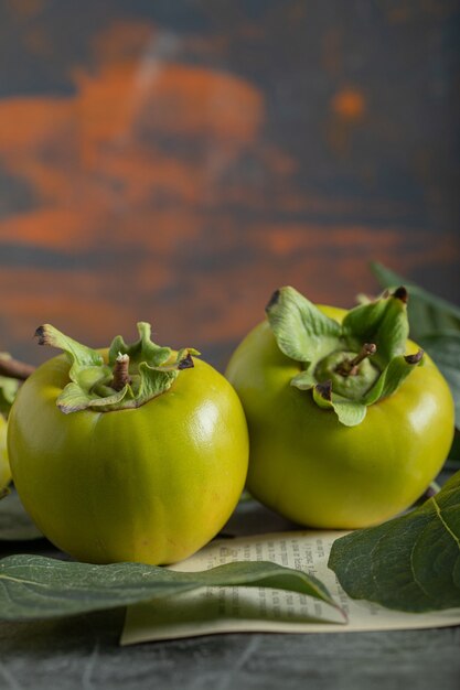 Unripe persimmons with leaves on marble background