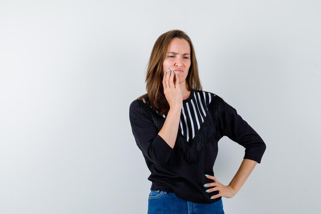 Unsatisfied young woman holding her hand on her cheek on white background