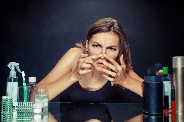 Unsatisfied young woman looking at her self in mirror on black wall