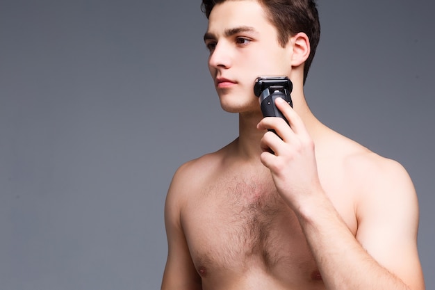 Unshaven man with naked torso looking forward to, and using trimmer