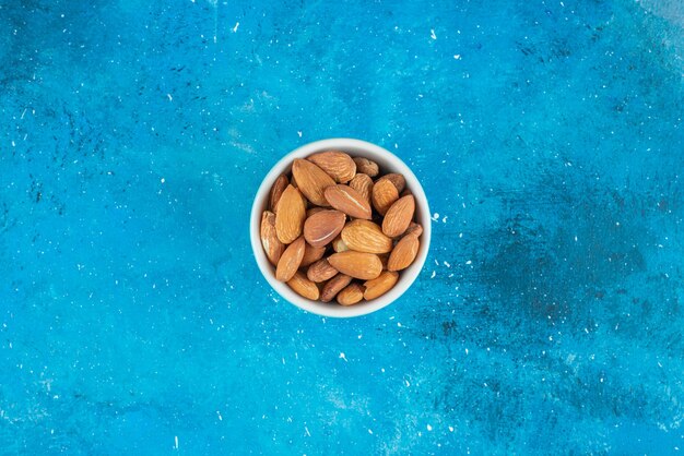 Unshelled almonds in a bowl on the blue surface