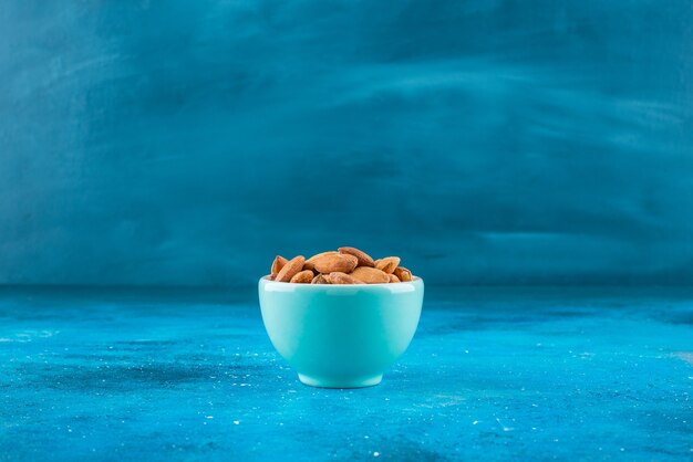 Unshelled almonds in a bowl, on the blue table. 