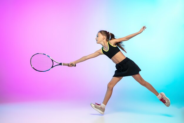 Unstoppable. Little tennis girl in black sportwear isolated on gradient wall