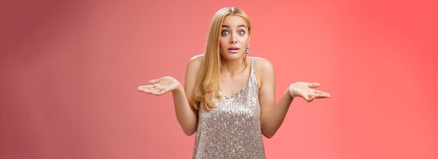 Unsure clueless awkward attractive blond european woman in silver glamour dress shrugging hands side