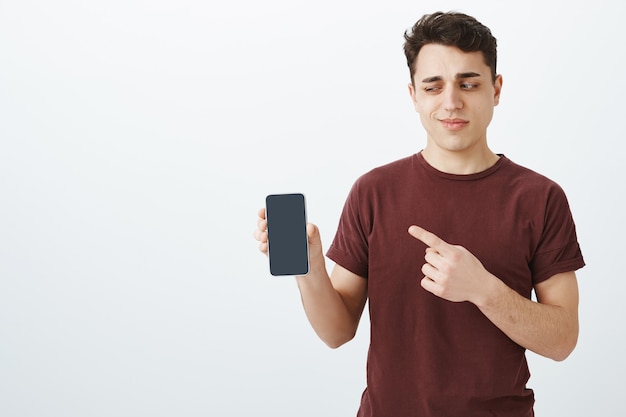 unsure doubtful male customer in red t-shirt showing a new smartphone