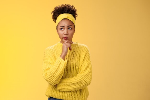 Unsure hesitant worried cute african-american girl face tough decision look up thoughtful make plan thinking how act right touch chin, make assumption standing concerned yellow background.