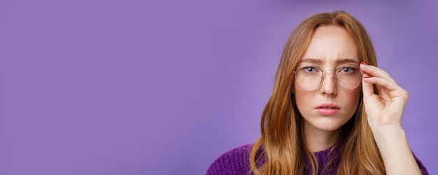 Unsure and seriouslooking focused redhead woman frowning and squinting as looking in prescribed glas