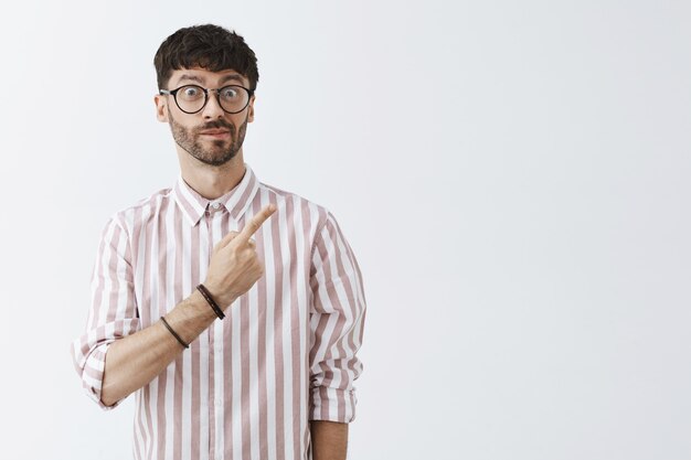 Unsure stylish bearded guy posing against the white wall with glasses