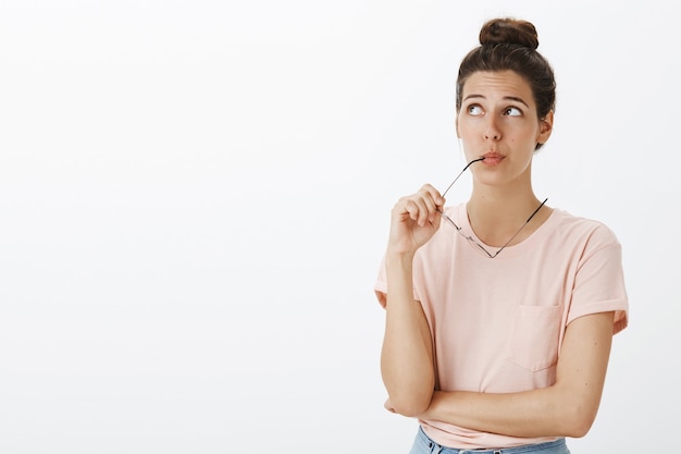 Unsure thoughtful girl with glasses posing against the white wall