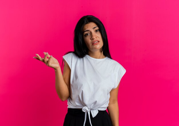 Unsure young caucasian girl stands with open hands isolated on pink background with copy space