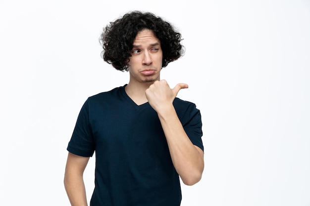 Free photo unsure young handsome man looking and pointing at side isolated on white background