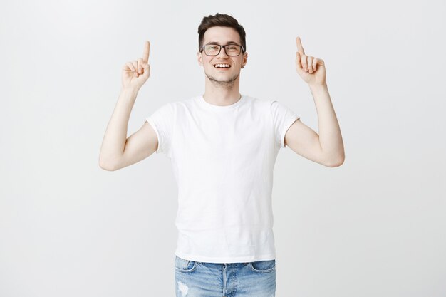 Free photo upbeat handsome young man in glasses pointing fingers up