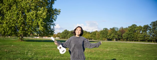 無料写真 楽器を弾いて踊る若い女性がウクレレを上げて公園でポーズをとる