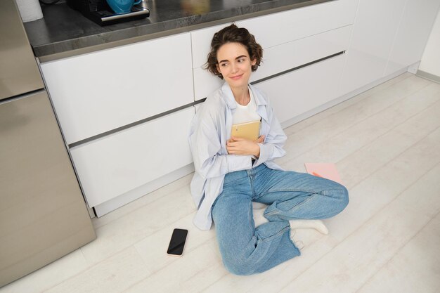 Upper angle shot of young woman sitting on kitchen floor revising for exam reading her notes doing h